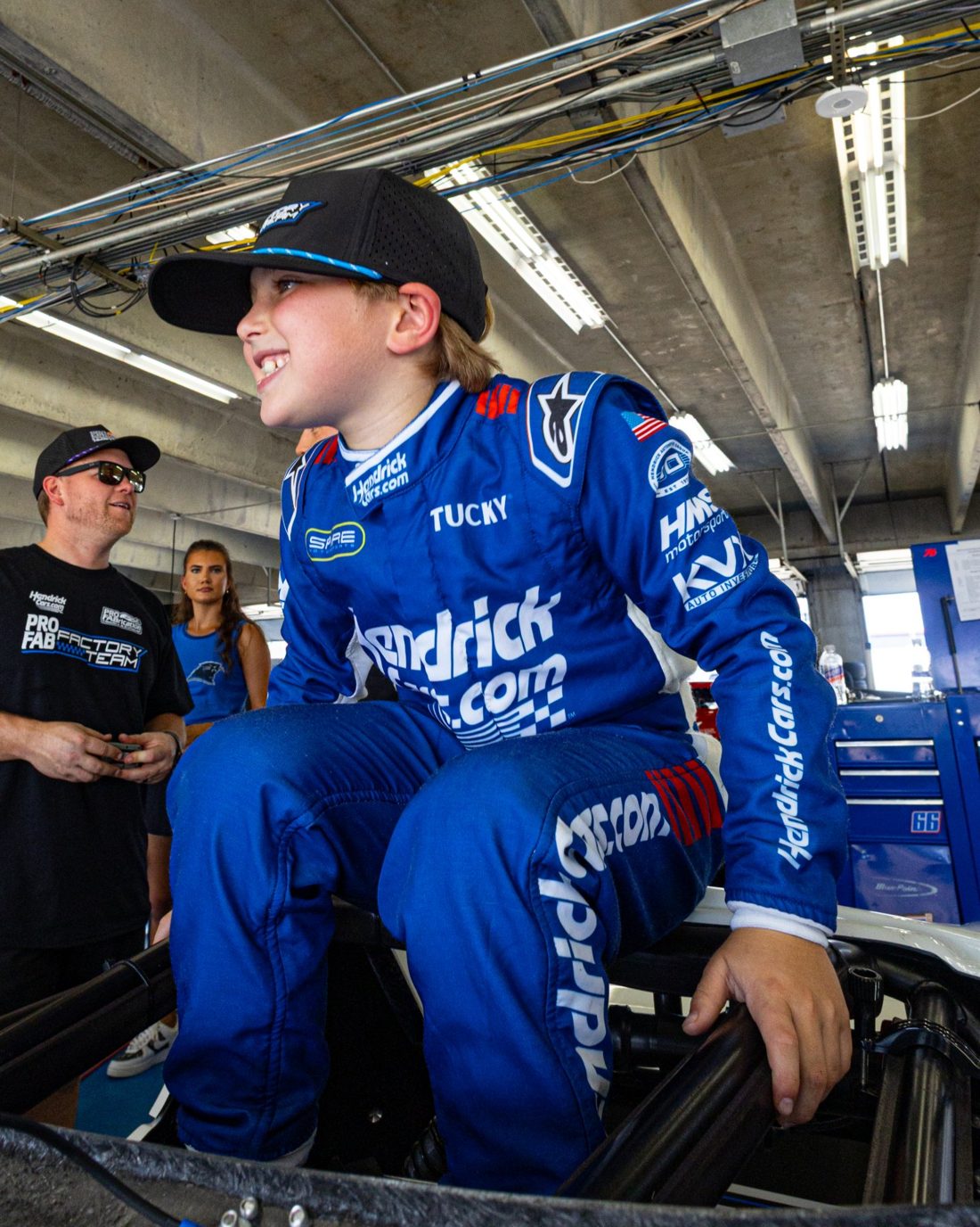 Kip grinning as he climbs into his Bandolero in the garage, in his HendrickCars.com fire suit and Factory Team hat