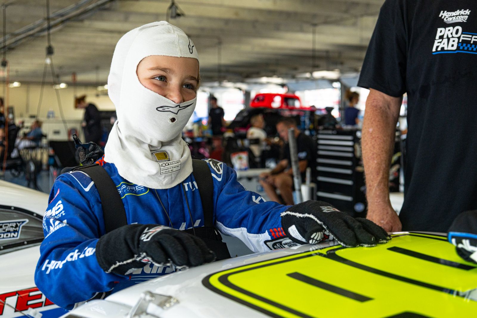 Kip in a white balaclava and gloves, smiling and leaning on the car roof