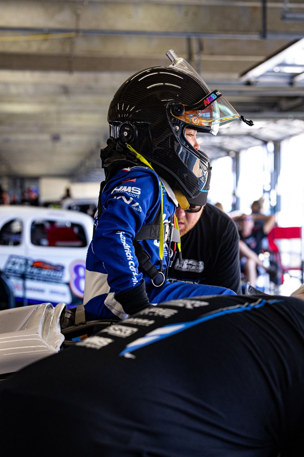 Kip in profile, helmet on, as the ProFab crew works on the car
